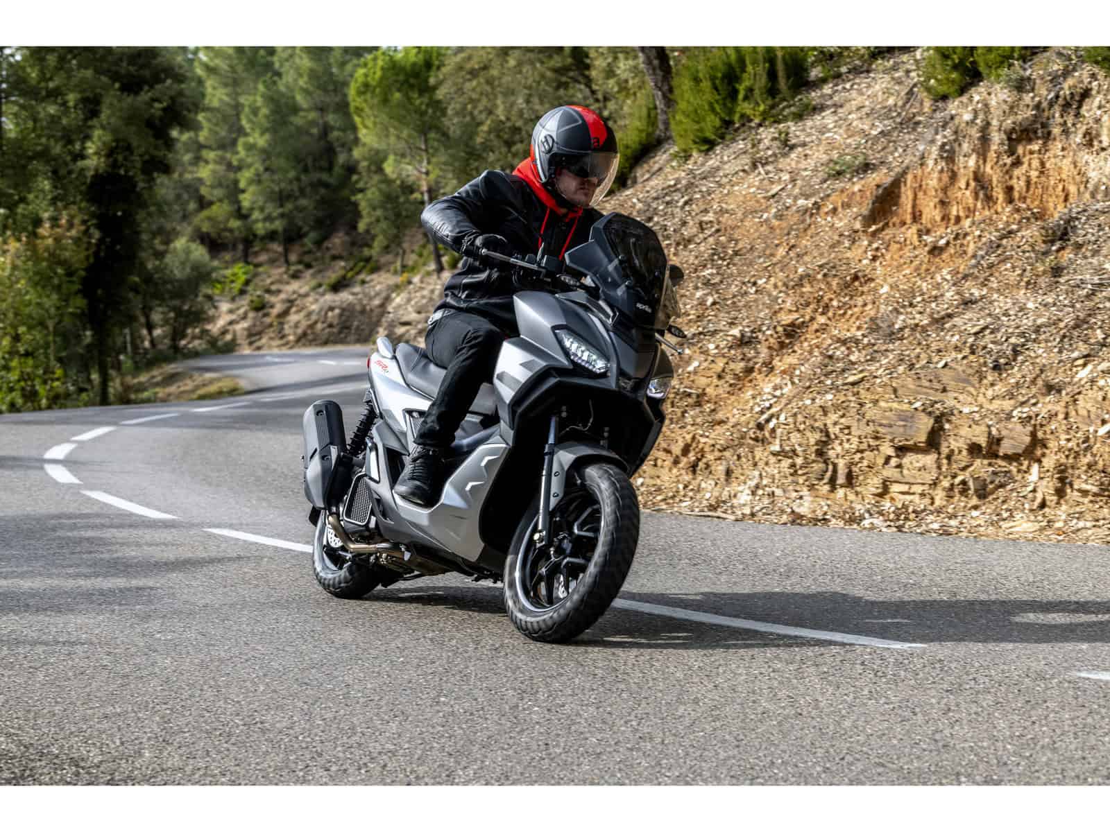 Ein Motorradfahrer fährt auf einer kurvenreichen Straße. Der Fahrer trägt eine schwarze Jacke und einen schwarzen Helm mit roten Akzenten.