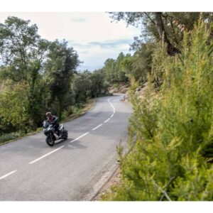 Ein Motorradfahrer fährt auf einer kurvenreichen Straße durch eine grüne Landschaft. Der Fahrer trägt Schutzkleidung.